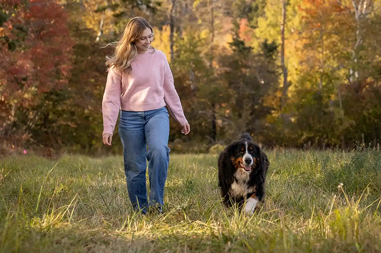 Frau lächelnd in Gras sitzend mit Staffordshire Terrier